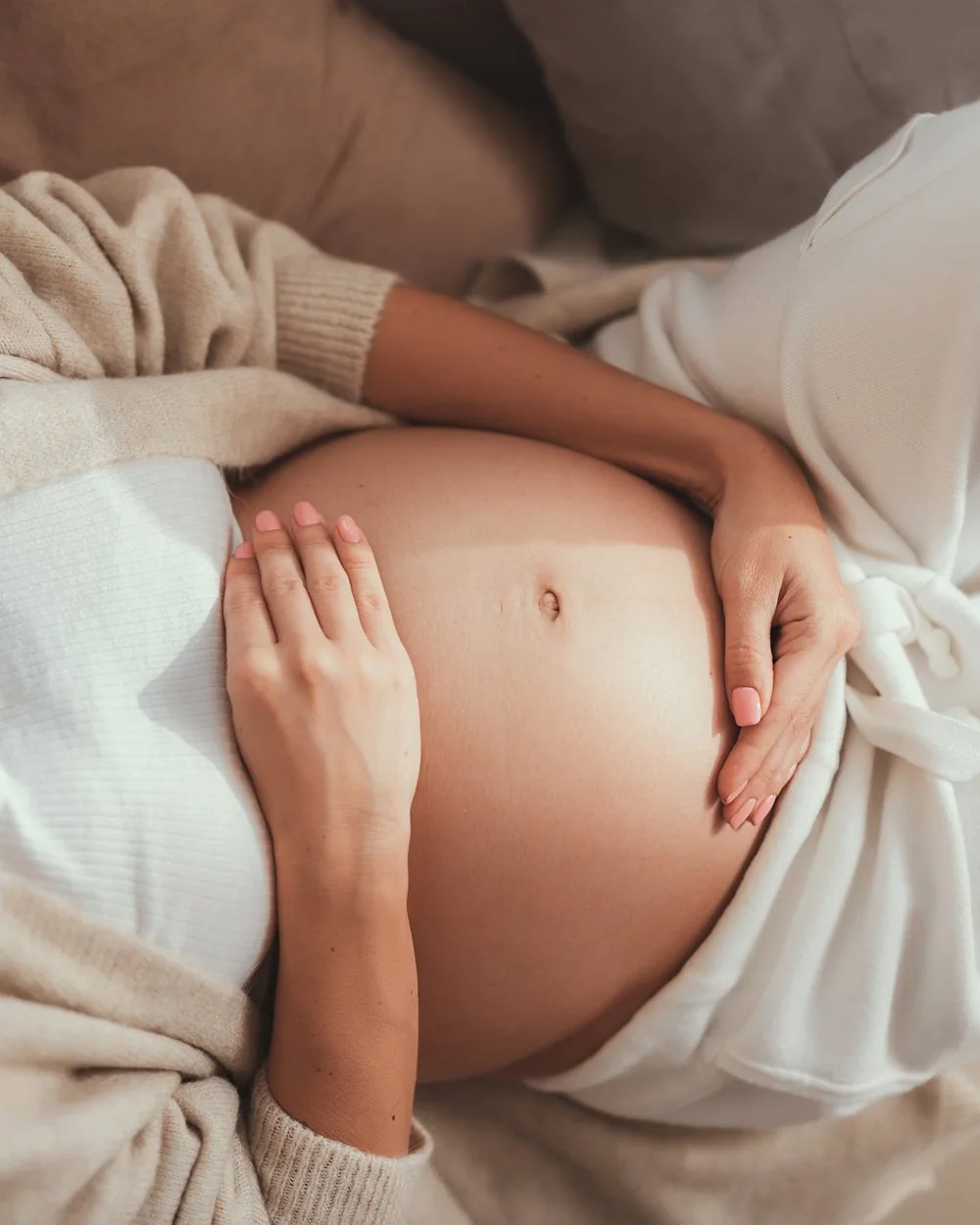 Expectant mother resting with both hands on her belly in the third trimester